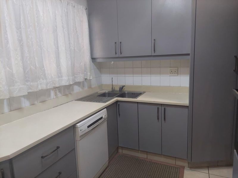 A functional kitchen featuring grey built-in cabinetry, laminate countertops, a stainless steel double sink, and a tiled backsplash.