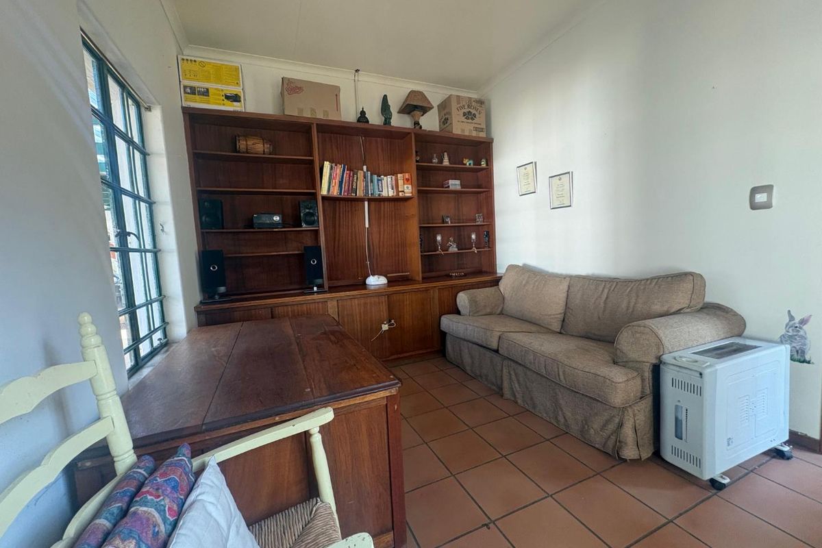 A living room featuring built-in wooden shelving, terracotta floor tiles, and a large steel-framed window, offering a functional and traditional space.