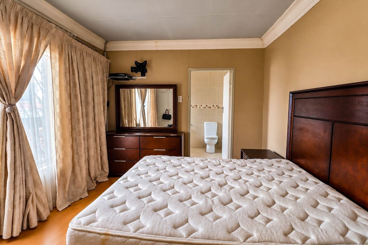 A bedroom featuring laminate flooring, crown molding, and an attached en-suite bathroom with a toilet visible.