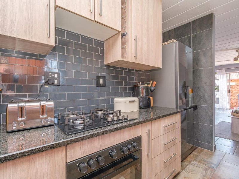 Modern kitchen featuring light wood cabinetry, granite countertops, a gas hob, built-in oven, and stylish dark subway tile backsplash.