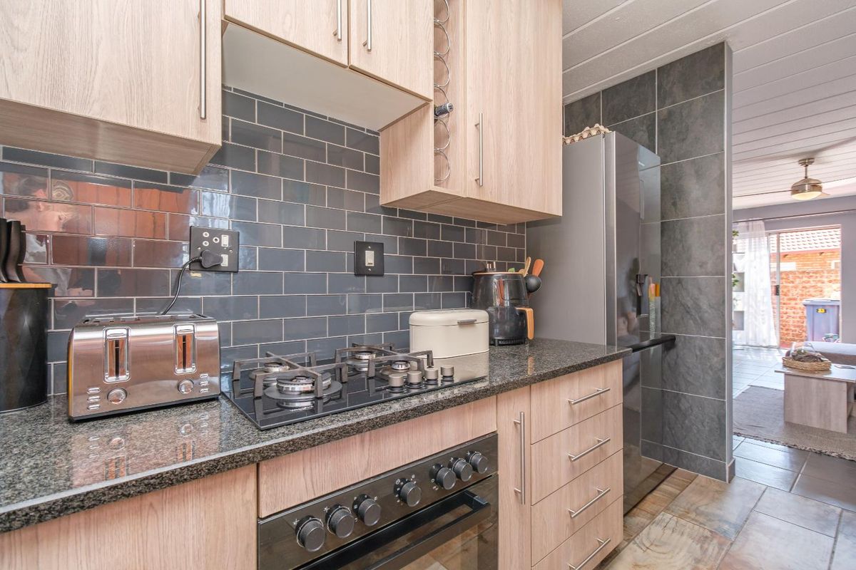 Modern kitchen featuring light wood cabinetry, granite countertops, a gas hob, built-in oven, and stylish dark subway tile backsplash.