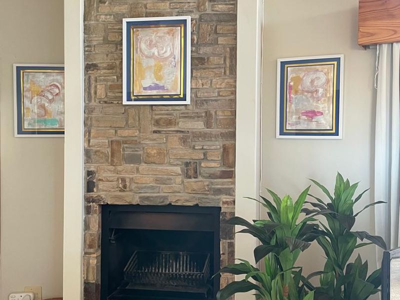 A cozy living room area featuring a prominent stone fireplace, tiled flooring, and exposed timber ceiling beams.