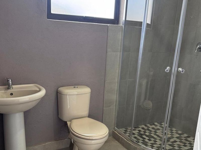 A functional bathroom featuring a pedestal basin, a standard toilet, and a corner shower enclosure with tiled finishes.