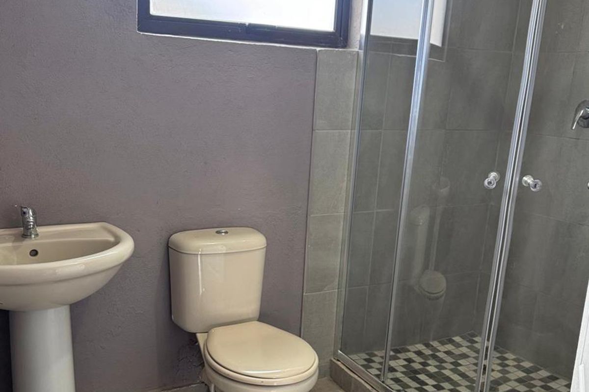 A functional bathroom featuring a pedestal basin, a standard toilet, and a corner shower enclosure with tiled finishes.