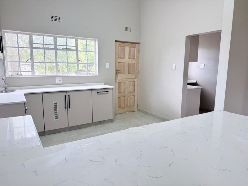 Modern kitchen featuring clean quartz countertops, ample built-in cabinetry, tiled flooring, and a bright window, offering a functional and neutral space.