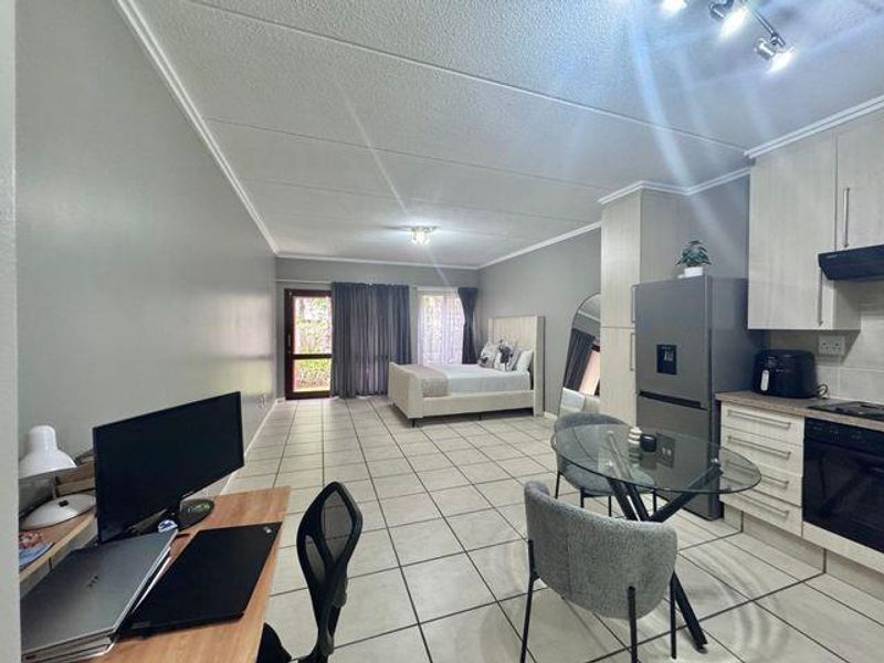 Open-plan studio apartment featuring a functional kitchen with built-in cabinetry, tiled flooring throughout, and direct access to an outdoor area via a sliding door.