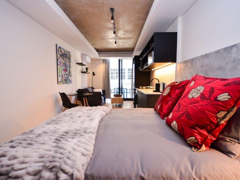 Modern open-plan studio apartment featuring an exposed concrete ceiling, integrated kitchen cabinetry, and direct access to a private balcony.