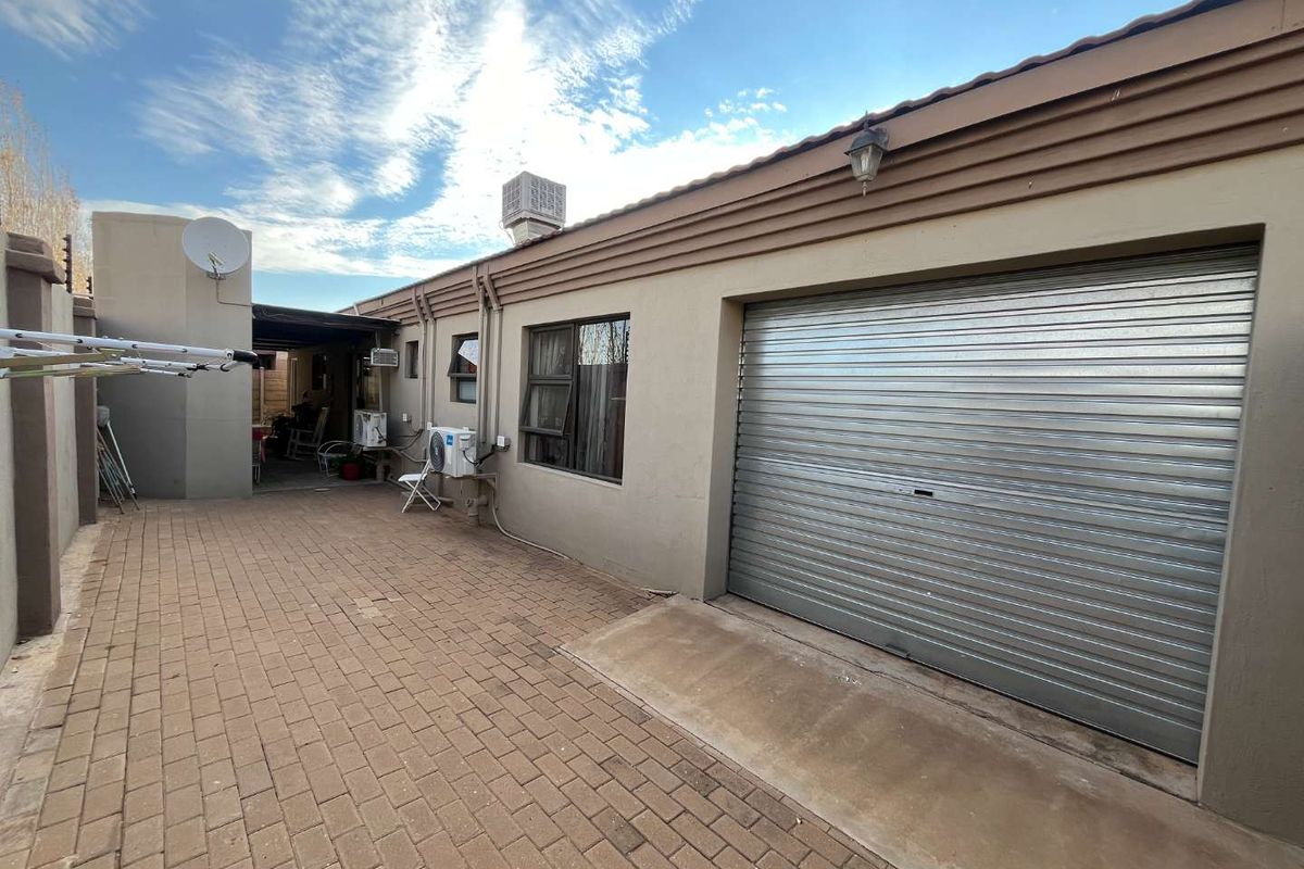 Rear exterior view of the townhouse featuring a paved courtyard, a roller garage door, and an attached covered patio area.