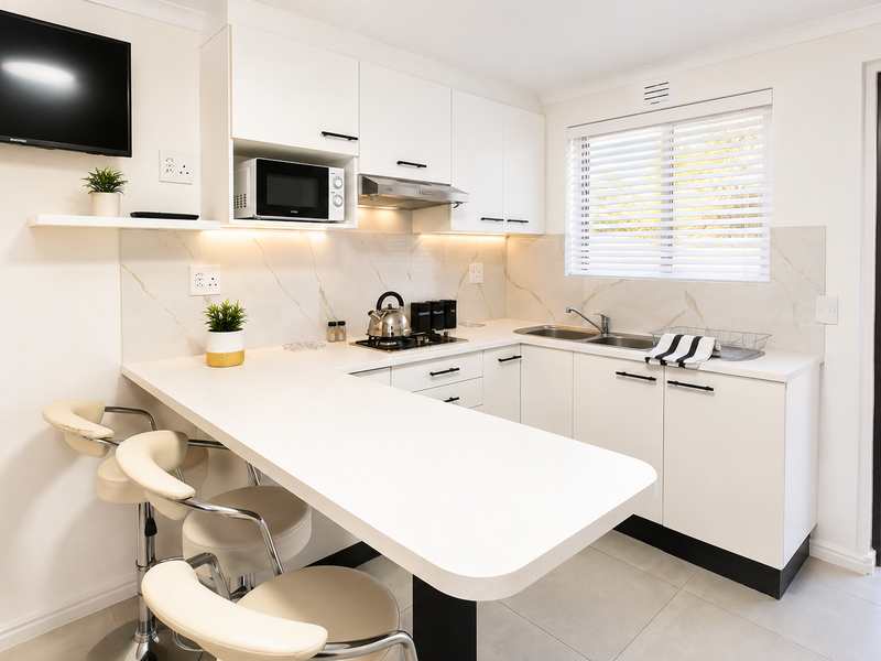 Modern, well-appointed kitchen featuring white cabinetry, stone-look backsplash, integrated appliances, and a convenient breakfast bar with direct access to the outdoor patio area.