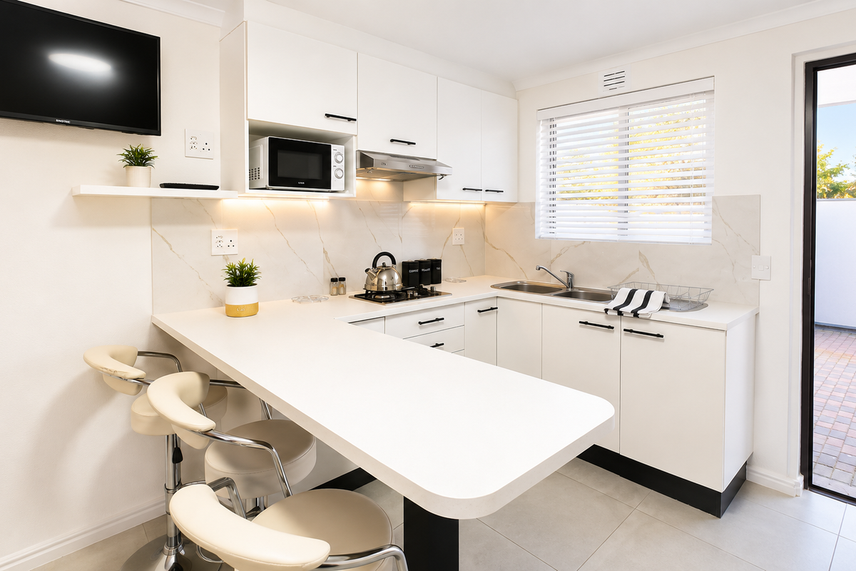Modern, well-appointed kitchen featuring white cabinetry, stone-look backsplash, integrated appliances, and a convenient breakfast bar with direct access to the outdoor patio area.