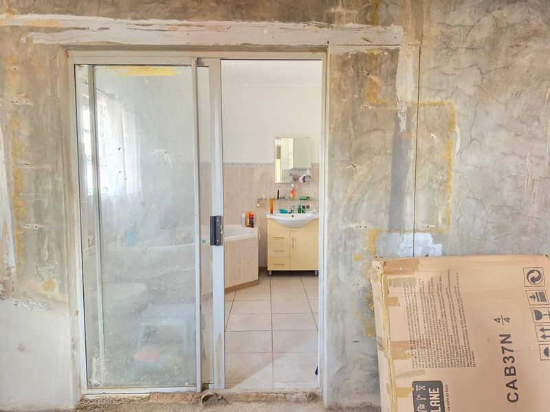 A bathroom viewed through a sliding door, featuring a vanity unit and bathtub, currently undergoing renovation with unfinished wall surfaces.