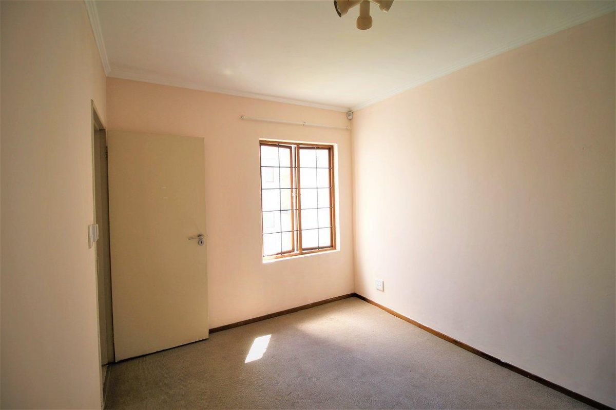 A vacant bedroom featuring neutral walls, carpeted flooring, and a window with security bars.