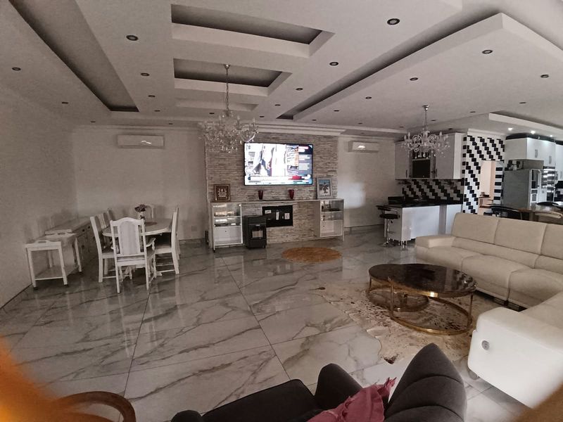 Spacious open-plan living and dining area featuring high-gloss marble-look flooring, a decorative tray ceiling, and a stone-clad feature wall with integrated media space.