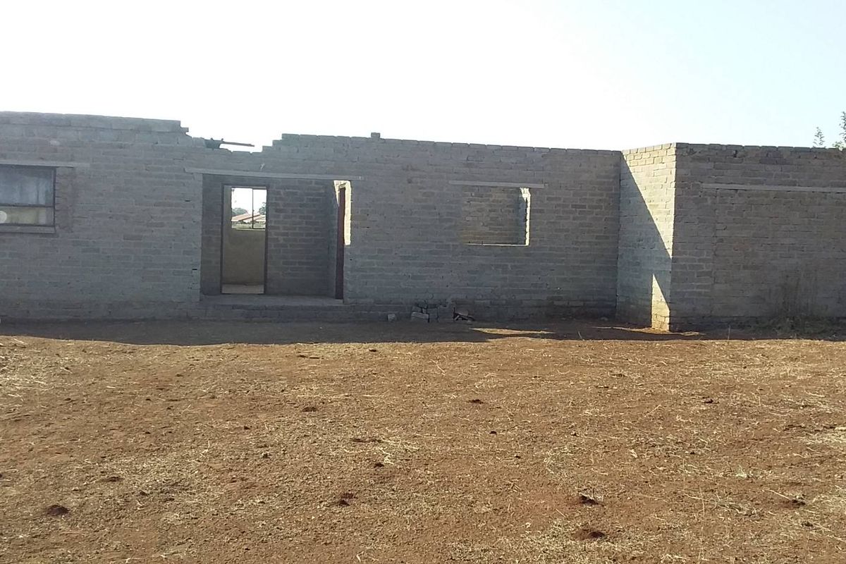 An unfinished residential structure showing exposed brick walls and open window and door frames on a vacant plot of land.