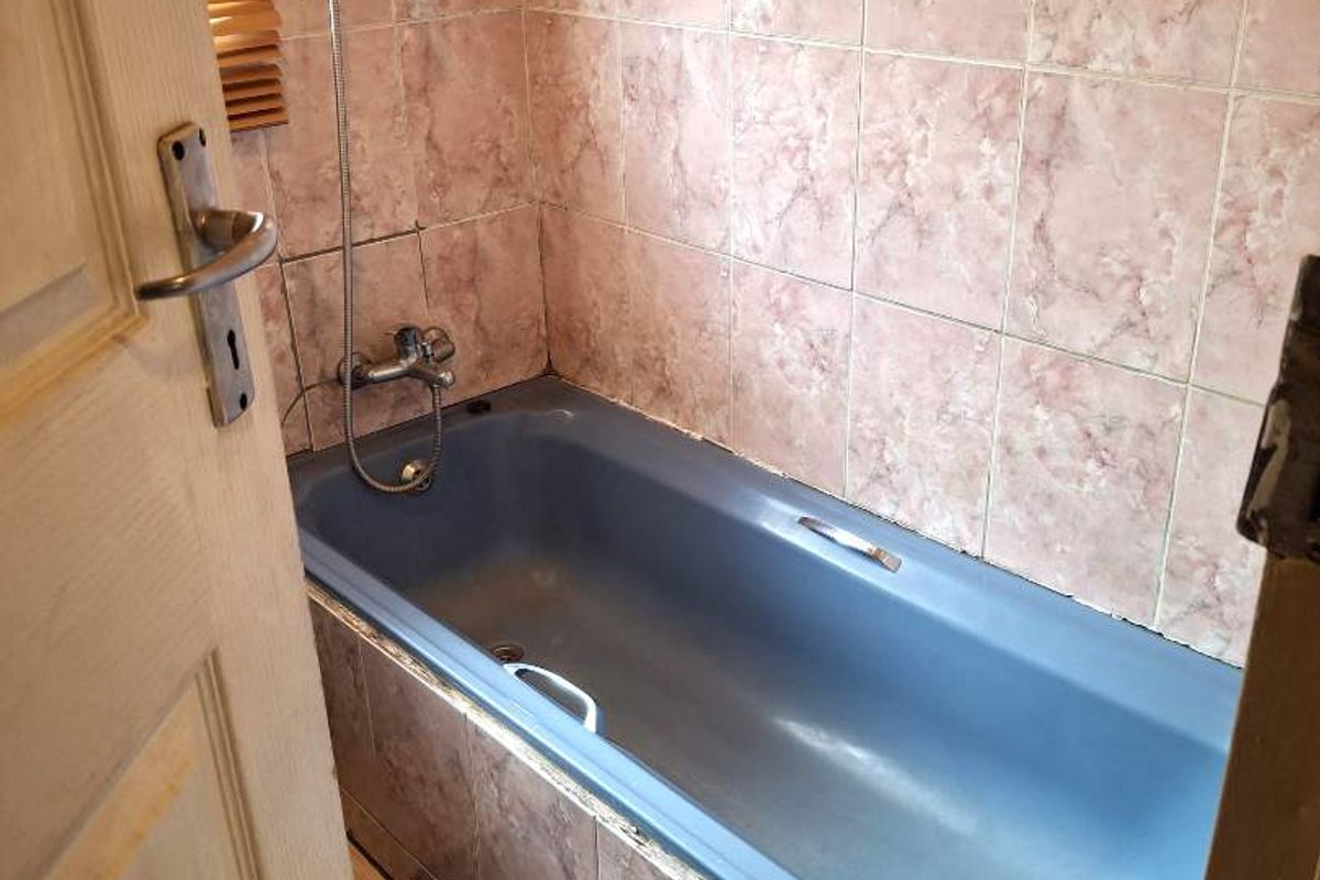 A compact bathroom featuring a blue bathtub with a handheld shower attachment and dated wall tiling.
