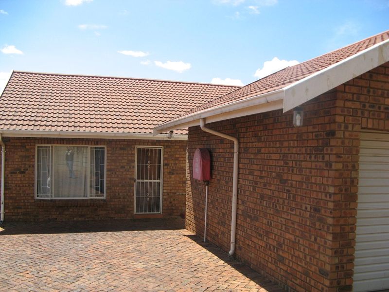 Front exterior view of a face brick townhouse featuring a paved driveway, tiled roof, and secure entrance with a security gate.