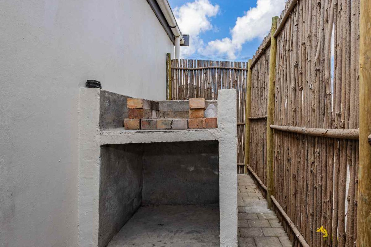 Outdoor area featuring a built-in masonry braai or barbecue structure, set against a side wall with rustic timber fencing.