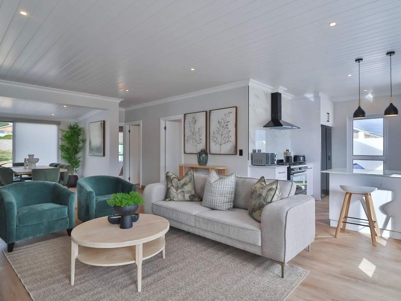 Modern open-plan living area featuring a contemporary kitchen with island, marble-look splashback, and light wood-tone flooring under a clean tongue and groove ceiling.