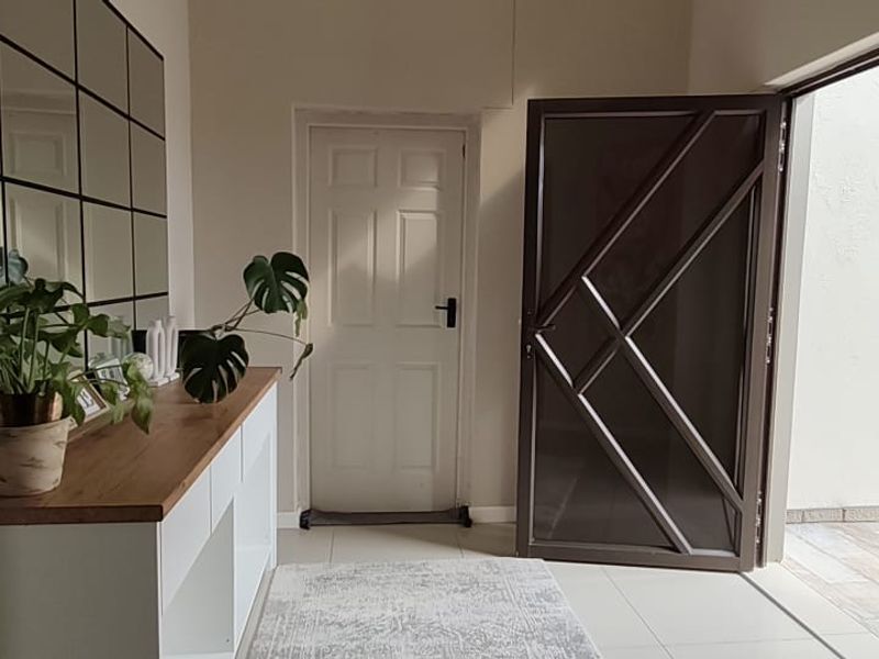 A bright entrance hall featuring tiled flooring, a decorative grid mirror, and a secure metal entrance gate leading to the exterior.