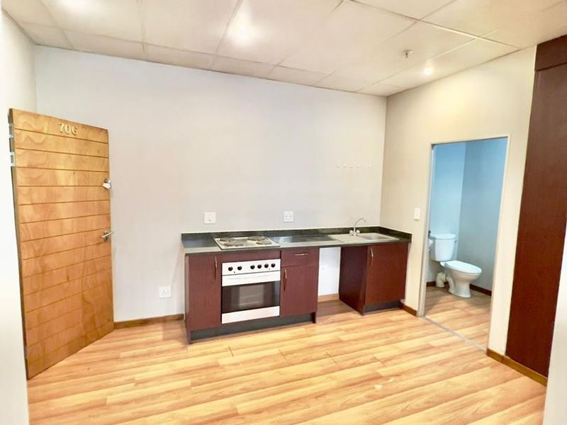 Open plan studio apartment featuring a kitchenette with built-in oven and hob, laminate flooring, and an attached bathroom.