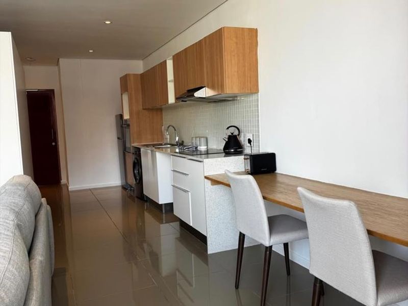 Modern open-plan kitchen featuring sleek cabinetry, stone countertops, and integrated appliances, seamlessly flowing into the living area with polished tiled flooring.