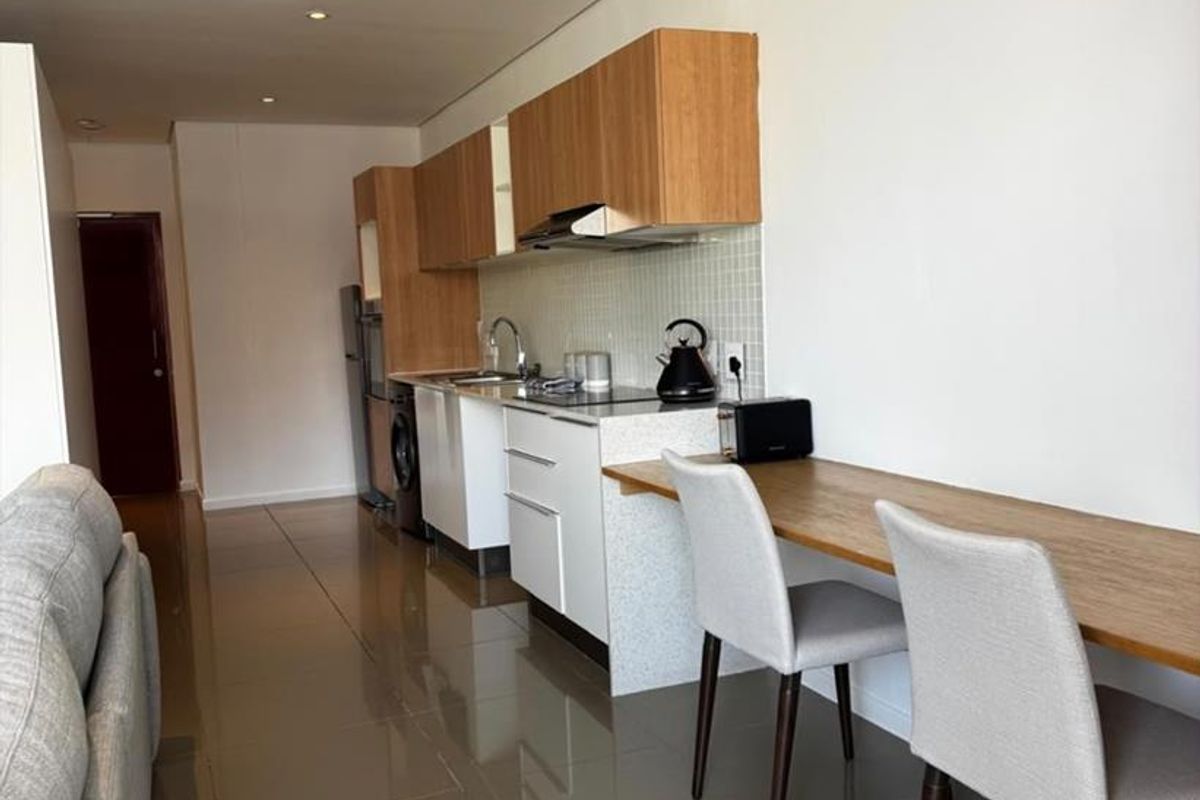 Modern open-plan kitchen featuring sleek cabinetry, stone countertops, and integrated appliances, seamlessly flowing into the living area with polished tiled flooring.