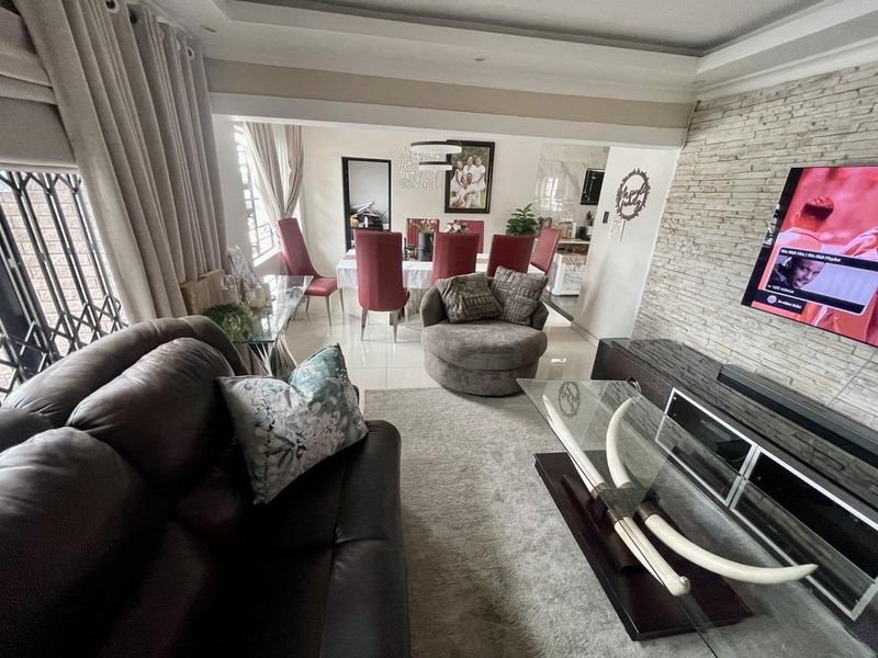 Open-plan living and dining area featuring a stone-clad feature wall, recessed ceiling details, and neutral tiled flooring throughout the connected space.