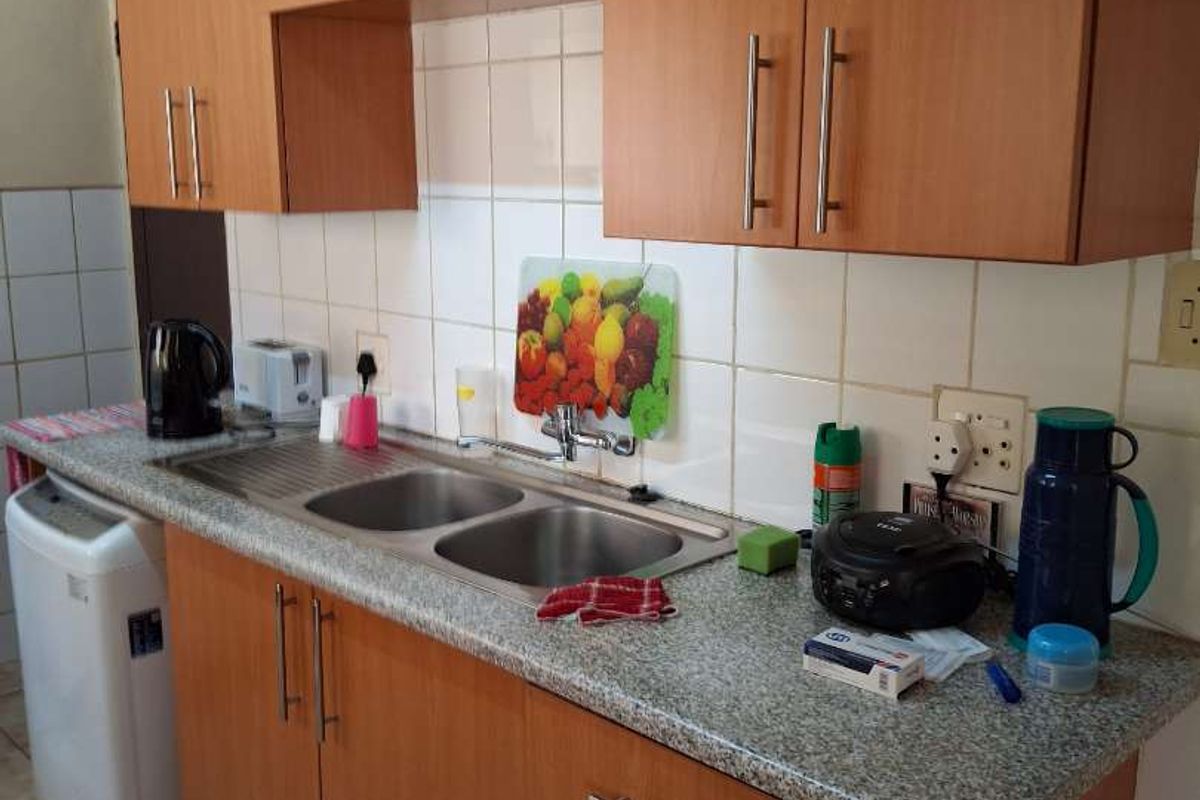 A functional kitchen area featuring wood-look laminate cabinetry, a double stainless steel sink, and tiled splashbacks.