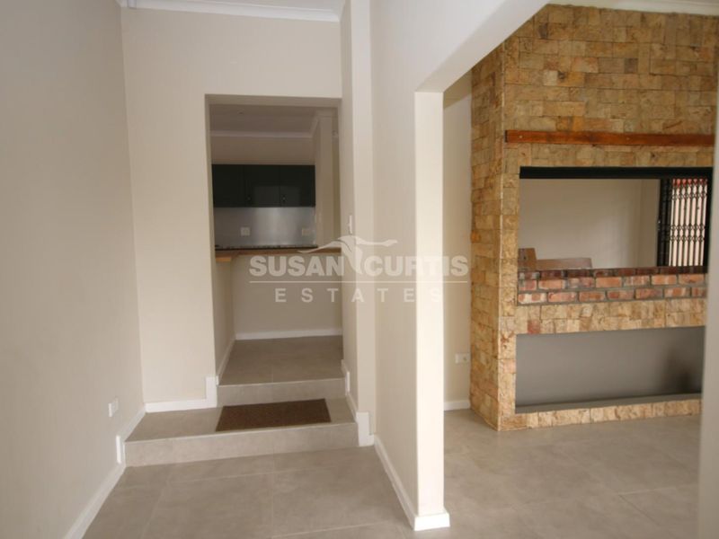 Spacious living area featuring a prominent stone-clad built-in fireplace and neutral tiled flooring, with a convenient pass-through opening to the kitchen area.