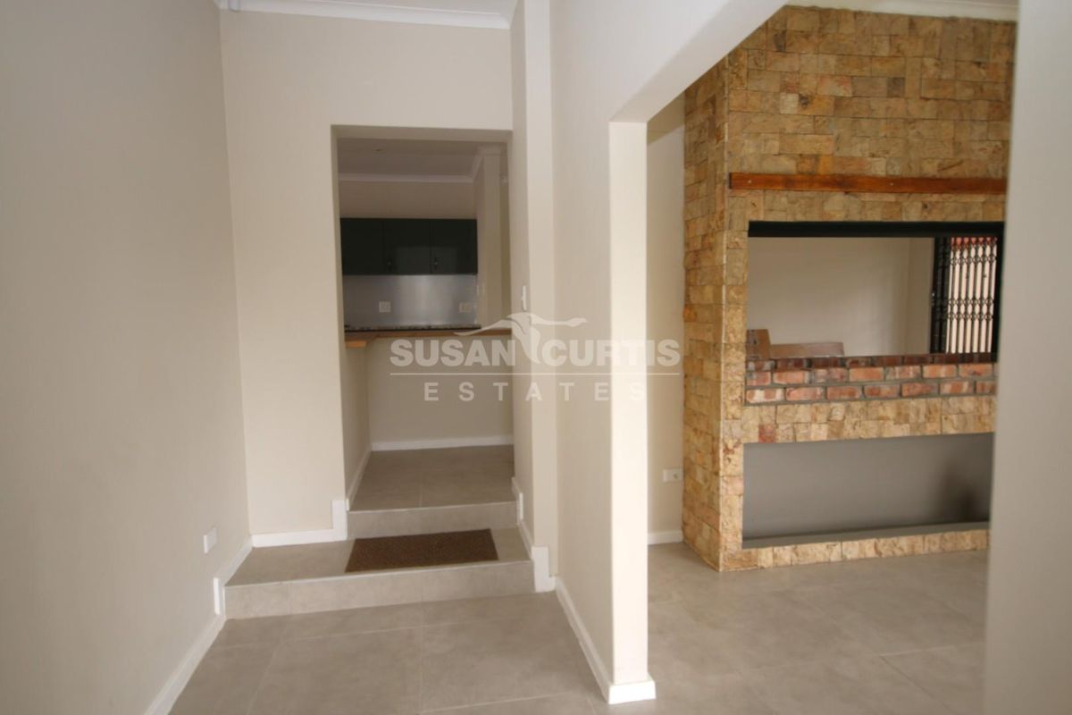 Spacious living area featuring a prominent stone-clad built-in fireplace and neutral tiled flooring, with a convenient pass-through opening to the kitchen area.