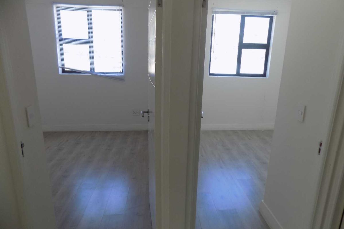 A view into two adjacent empty bedrooms featuring light-toned laminate flooring and neutral wall finishes.