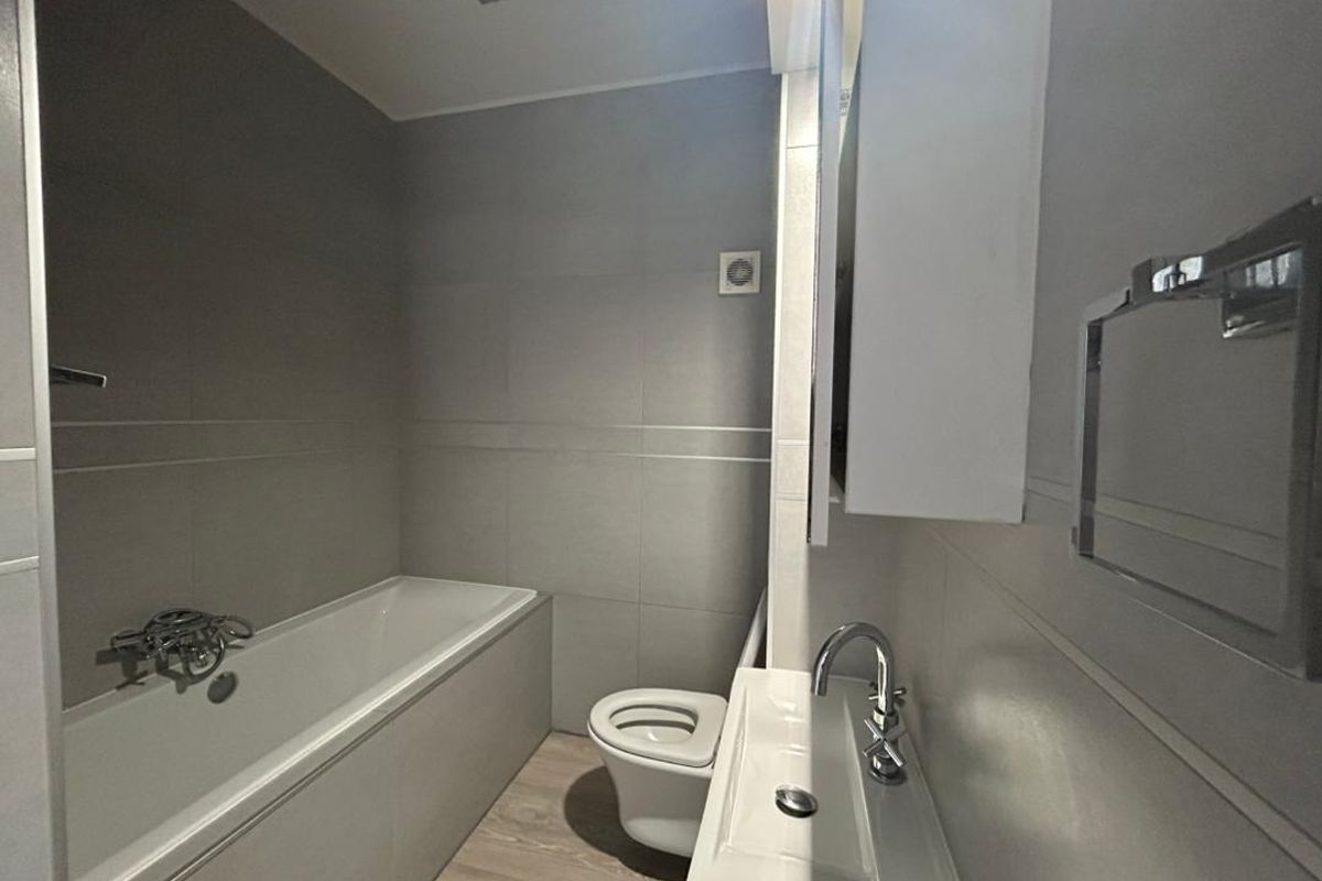 A modern, neutral-toned bathroom featuring a built-in bathtub, wall-mounted vanity basin, and integrated storage cabinet with clean, contemporary finishes.