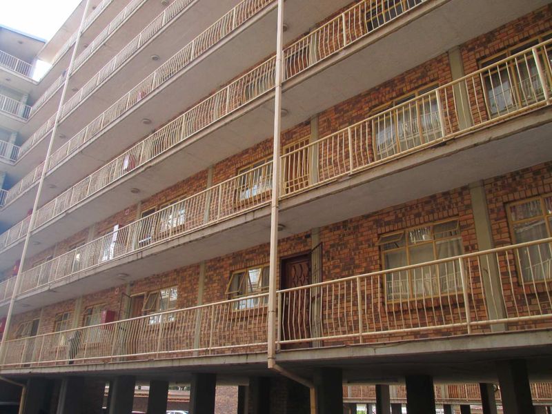 Exterior view of a multi-story apartment building featuring face brick facade, concrete balconies with metal railings, and security-fitted entrance doors.