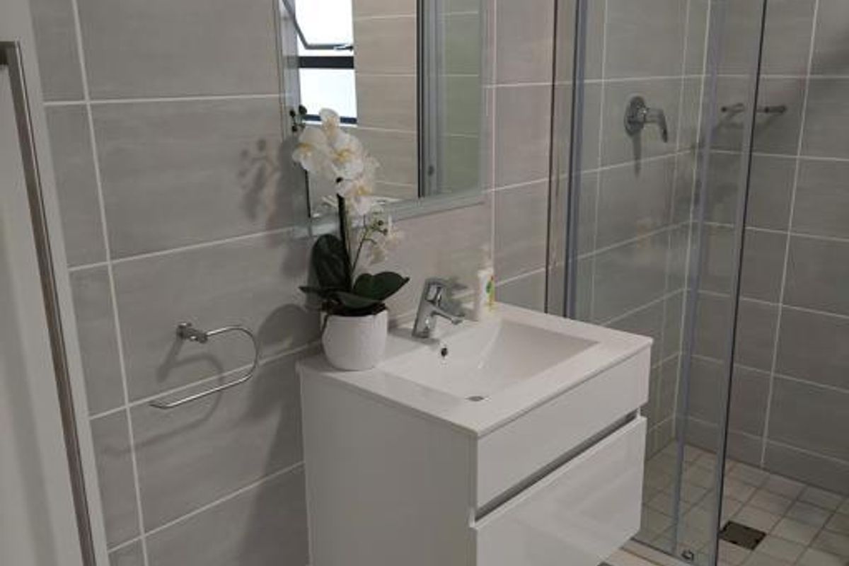 Modern bathroom featuring a wall-mounted vanity, glass-enclosed shower, and neutral grey wall and floor tiling.