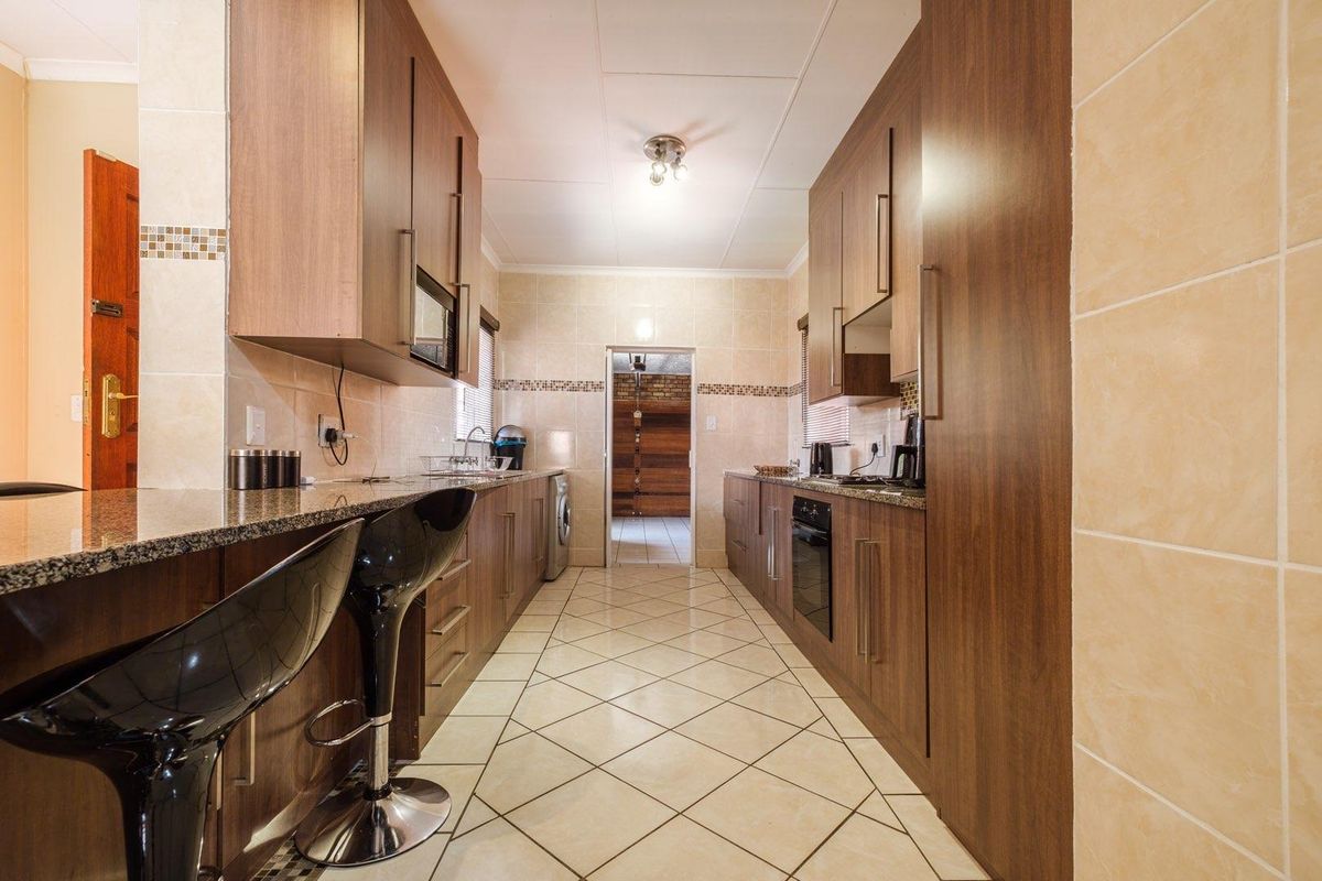 Galley-style kitchen featuring wood-finish cabinetry, granite countertops, built-in oven, and tiled flooring with a breakfast bar area.