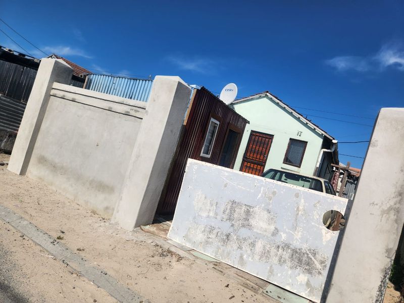 Front exterior view of a property featuring a concrete boundary wall, metal gate, and a small structure with corrugated metal siding.