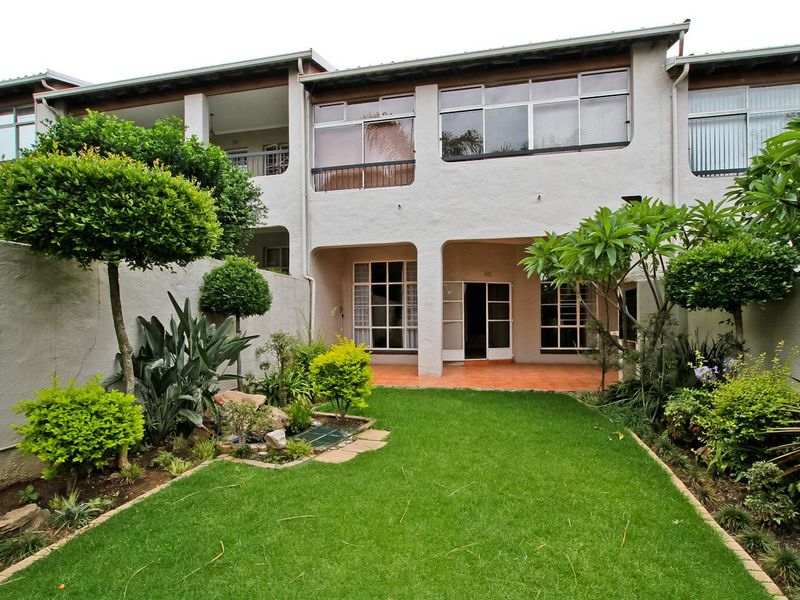 Rear view of the townhouse featuring a private landscaped garden, a covered patio area with tiled flooring, and large windows providing natural light.