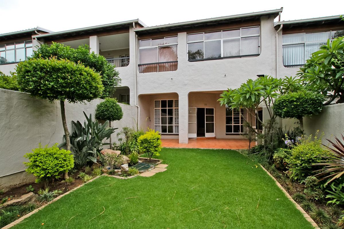 Rear view of the townhouse featuring a private landscaped garden, a covered patio area with tiled flooring, and large windows providing natural light.