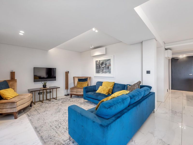 A modern, well-maintained living room featuring polished marble-look flooring, recessed ceiling lighting, and a wall-mounted air conditioning unit.