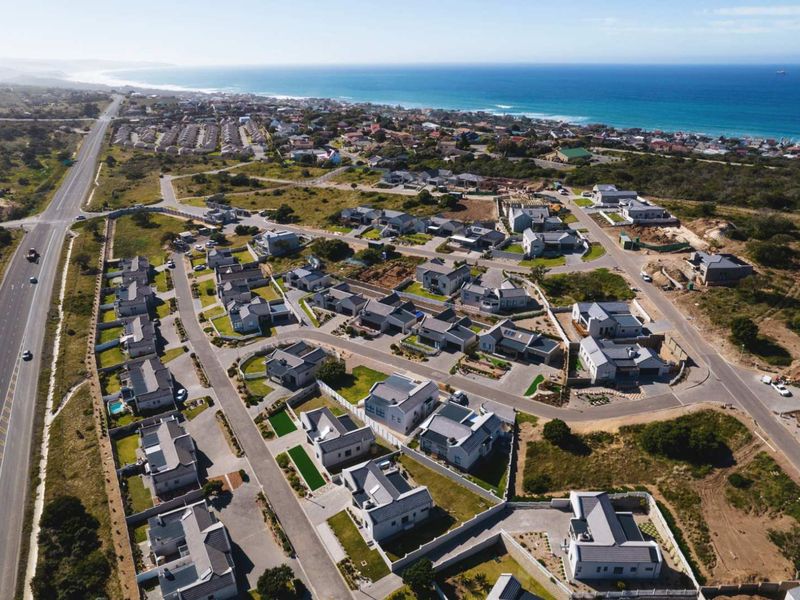An aerial view of a residential estate development located near the coastline, featuring multiple housing units and established road infrastructure.