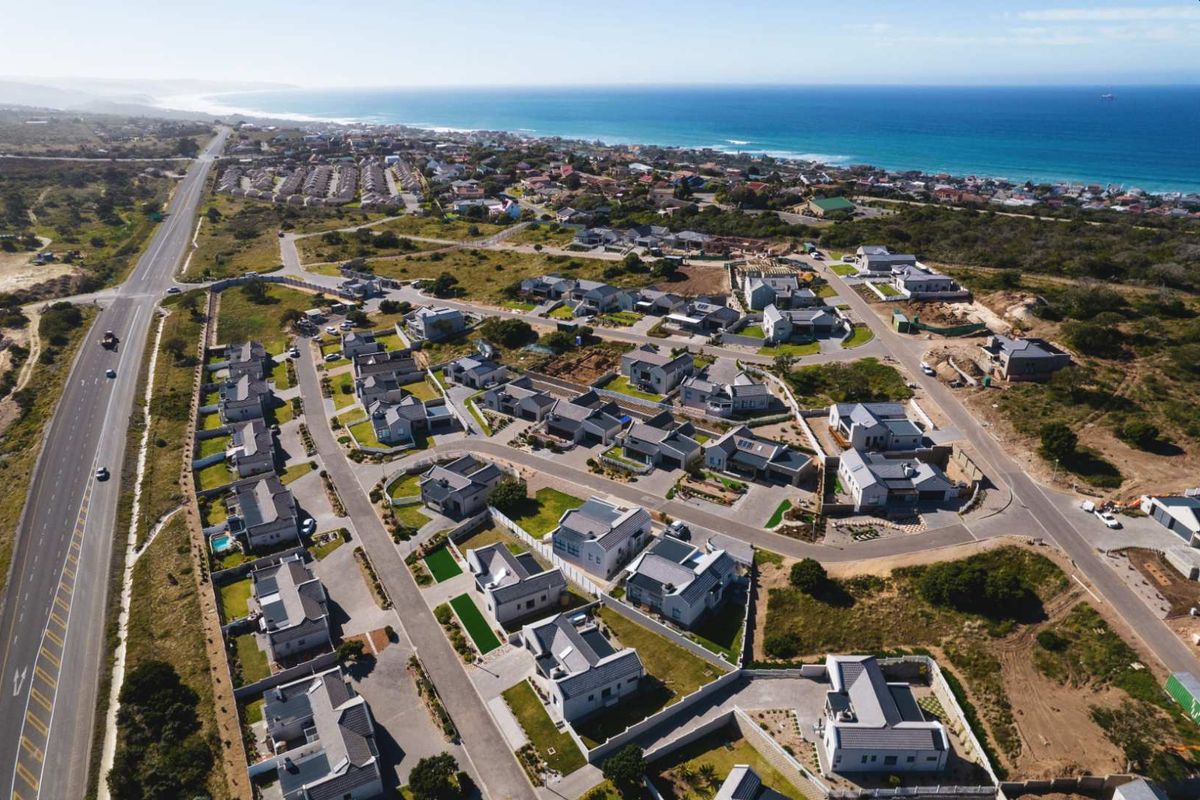An aerial view of a residential estate development located near the coastline, featuring multiple housing units and established road infrastructure.