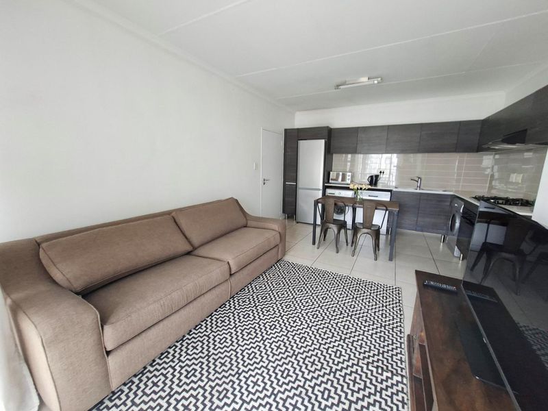 Open-plan living area featuring a modern kitchen with dark cabinetry, tiled flooring, and integrated appliances, seamlessly connected to the lounge space.