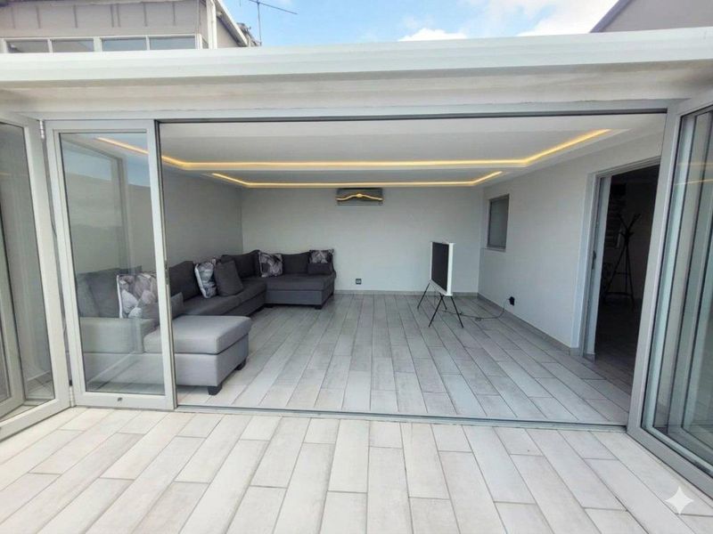 A modern, covered patio area featuring large sliding glass doors, recessed ceiling lighting, and a wall-mounted air conditioning unit, creating a seamless indoor-outdoor living space.