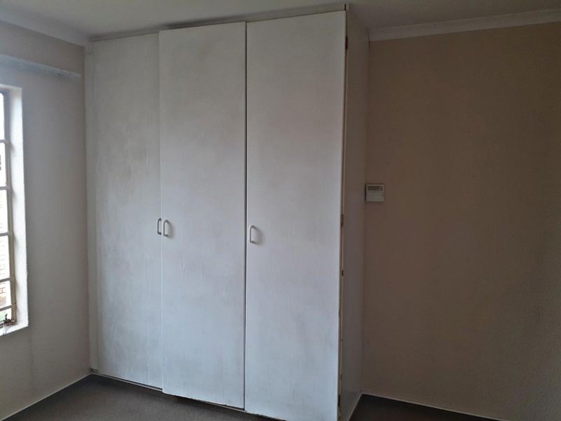 A bedroom featuring a built-in wardrobe with a basic finish, providing essential storage space within the room.