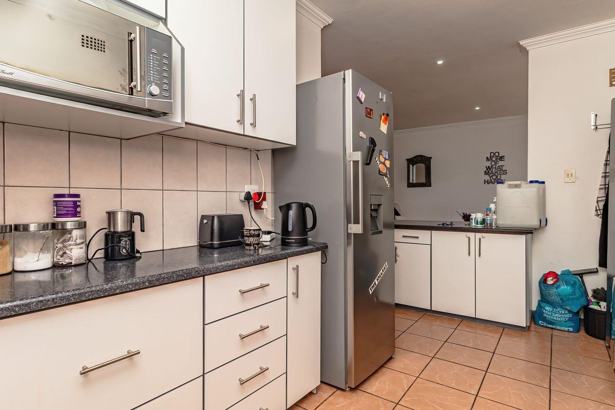 Functional kitchen featuring white cabinetry, dark laminate countertops, tiled backsplash, and built-in microwave, with adjacent utility area and tiled flooring.
