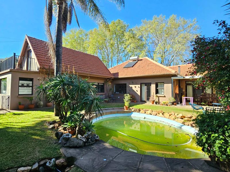 Rear view of the property featuring a swimming pool, landscaped garden, and a multi-level home with a tiled roof and balcony.