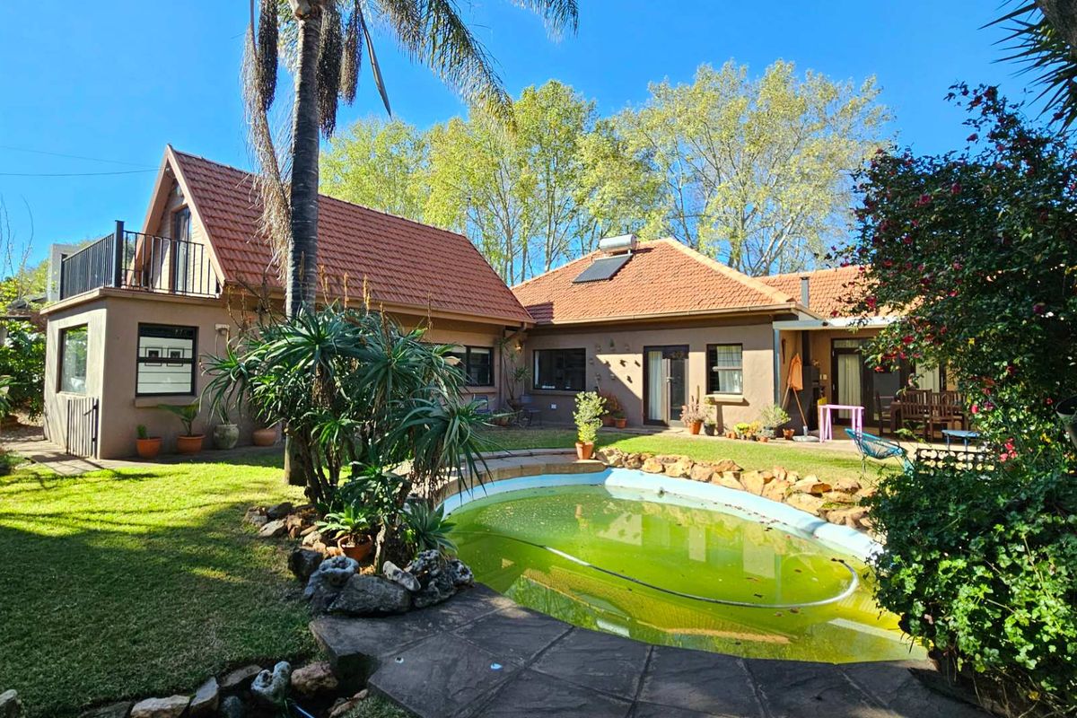 Rear view of the property featuring a swimming pool, landscaped garden, and a multi-level home with a tiled roof and balcony.