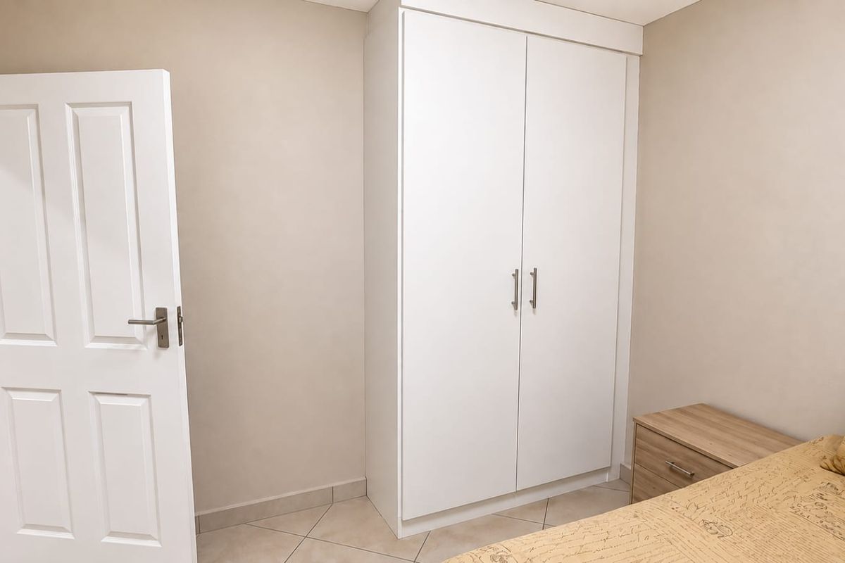 A clean bedroom featuring neutral wall tones, tiled flooring, and a white built-in wardrobe with modern hardware.