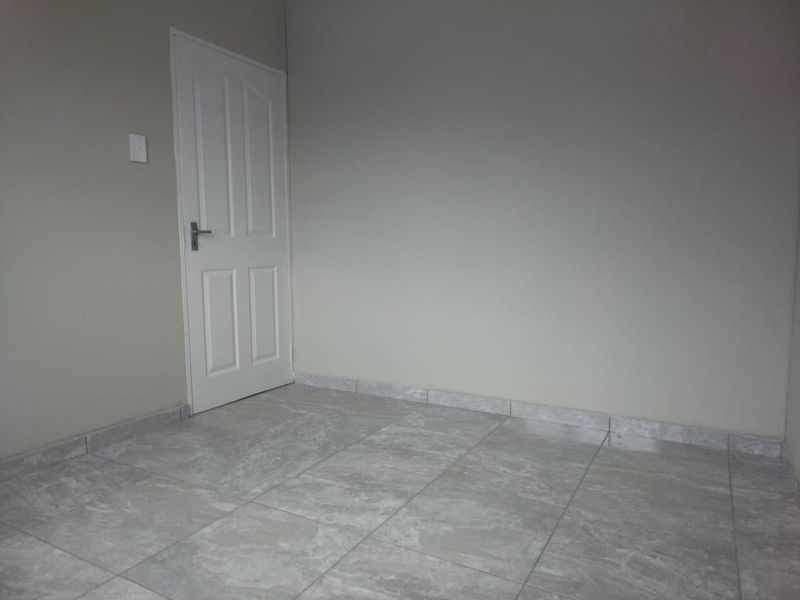 A clean, empty bedroom featuring neutral wall paint and modern grey tiled flooring with matching skirting boards.