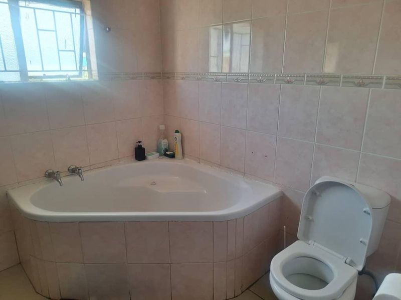 A functional bathroom featuring a corner bathtub, a standard toilet, and tiled walls. The space requires minor maintenance and cosmetic updates.